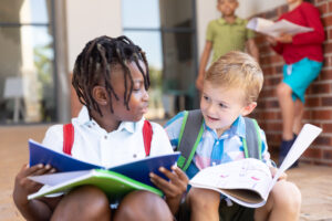 Two children sit on the steps in front of their elementary school