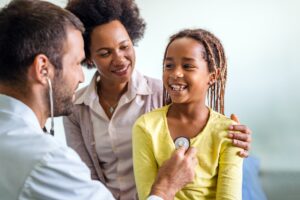 A doctor examines a healthy young African American girl in an exam room.