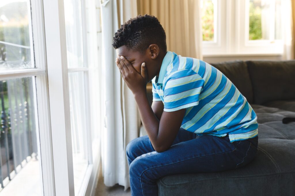 Sad African American boy sits on bed with his head in his hands