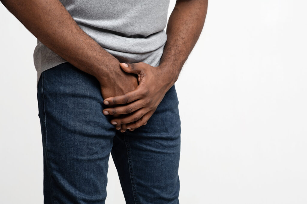 Cropped of black man holding his groin over white background, copy space