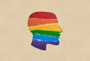 A cardboard background with the outline of a human head cut-out, revealing a rainbow colored LGBTQ+ support flag beneath