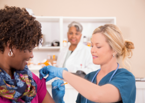 A woman smiles as she gets her annual flu shot from a nurse.