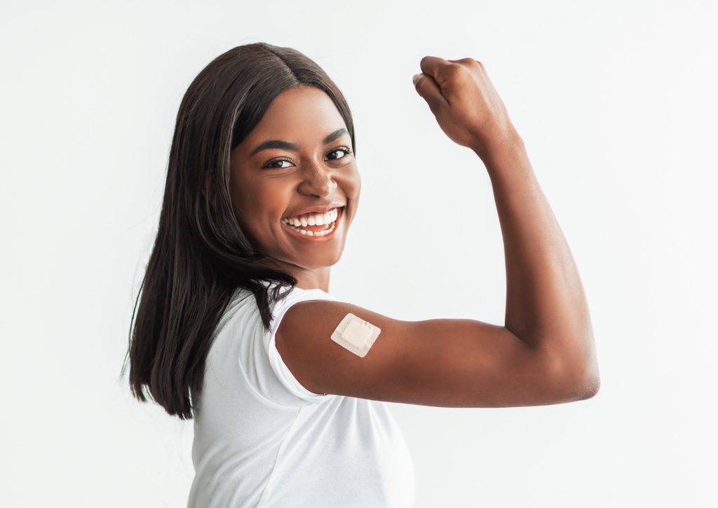 Smiling young woman showing a bandage on her arm after receiving a vaccine.