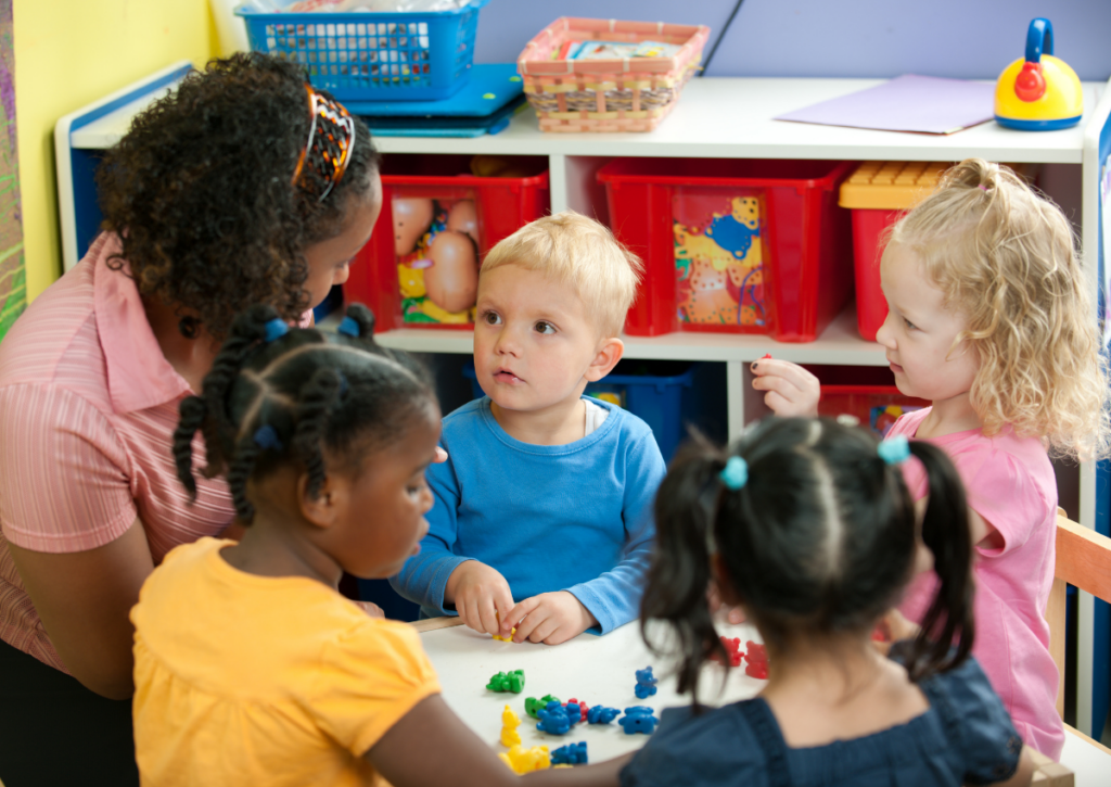 Young children and a teacher gathered around a classroom table.