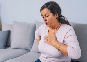 Woman sitting on a couch holding her chest and lower back while experiencing discomfort, illustrating possible heart attack symptoms in women.