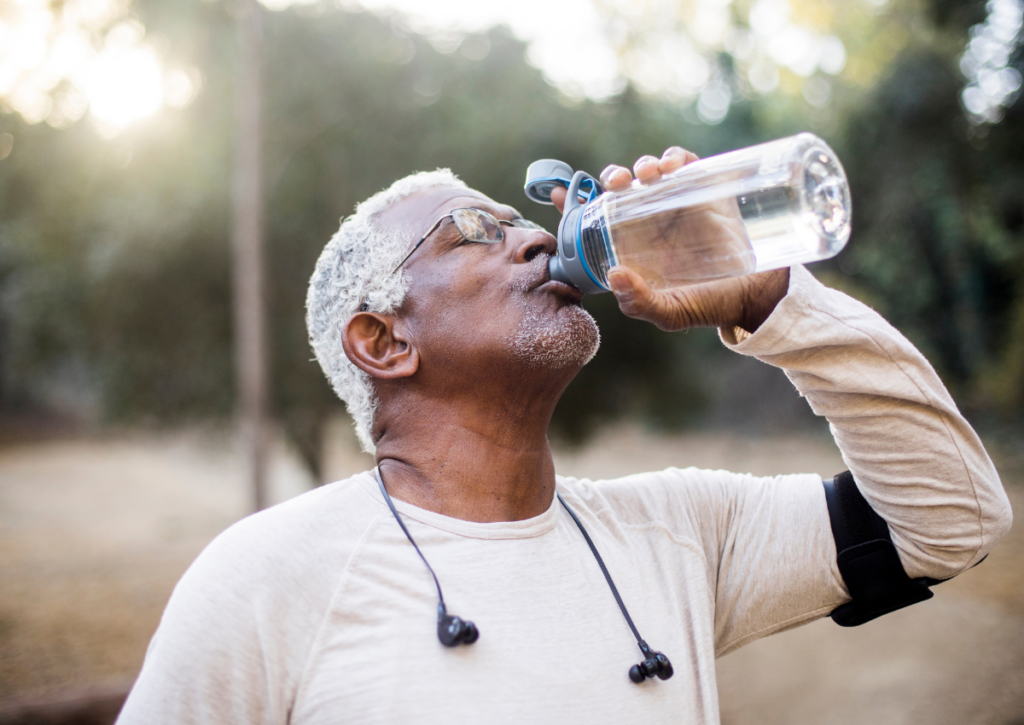 Older man drinking water from a reusable bottle outdoors.